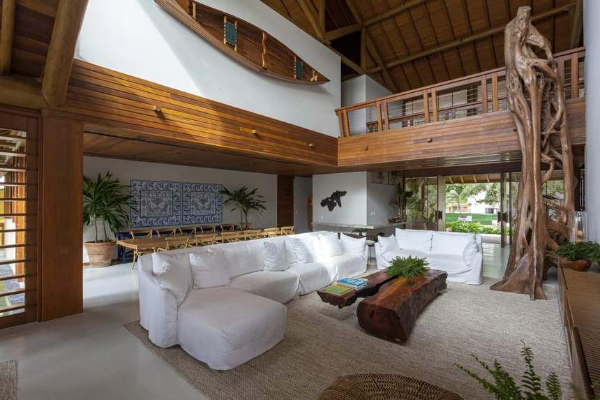 Living de pé-direito duplo, com estrutura de troncos aparente, canoa na parede e painel de azulejos ao fundo