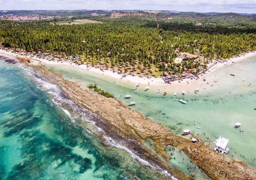 Vista aérea da Praia dos Carneiros — coqueiral, linha de recife exposta e lanchas fundeadas
