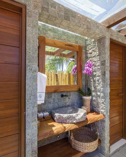 Lavabo externo com cuba de pedra bruta, orquídea e toalha bordada
