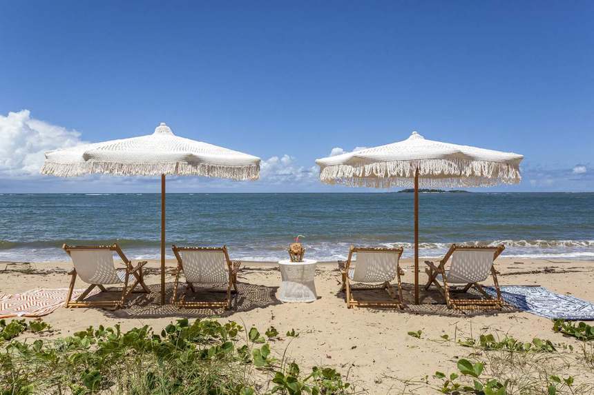 Praia privativa da Villa Capri, com ombrelones de crochê e a Ilha de Santo Aleixo no horizonte